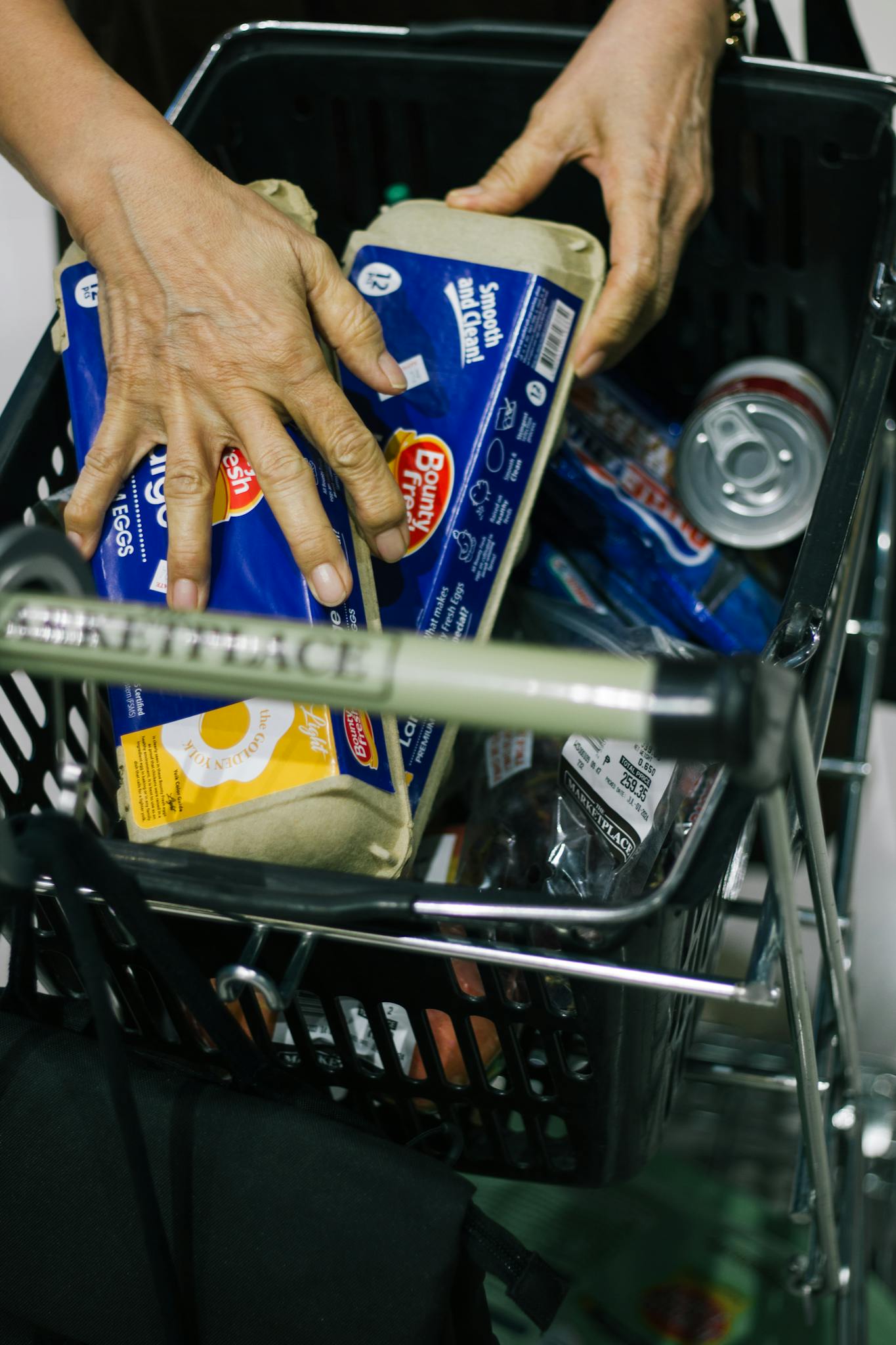 Adult placing groceries in a shopping cart at a store, emphasizing consumer activity.
