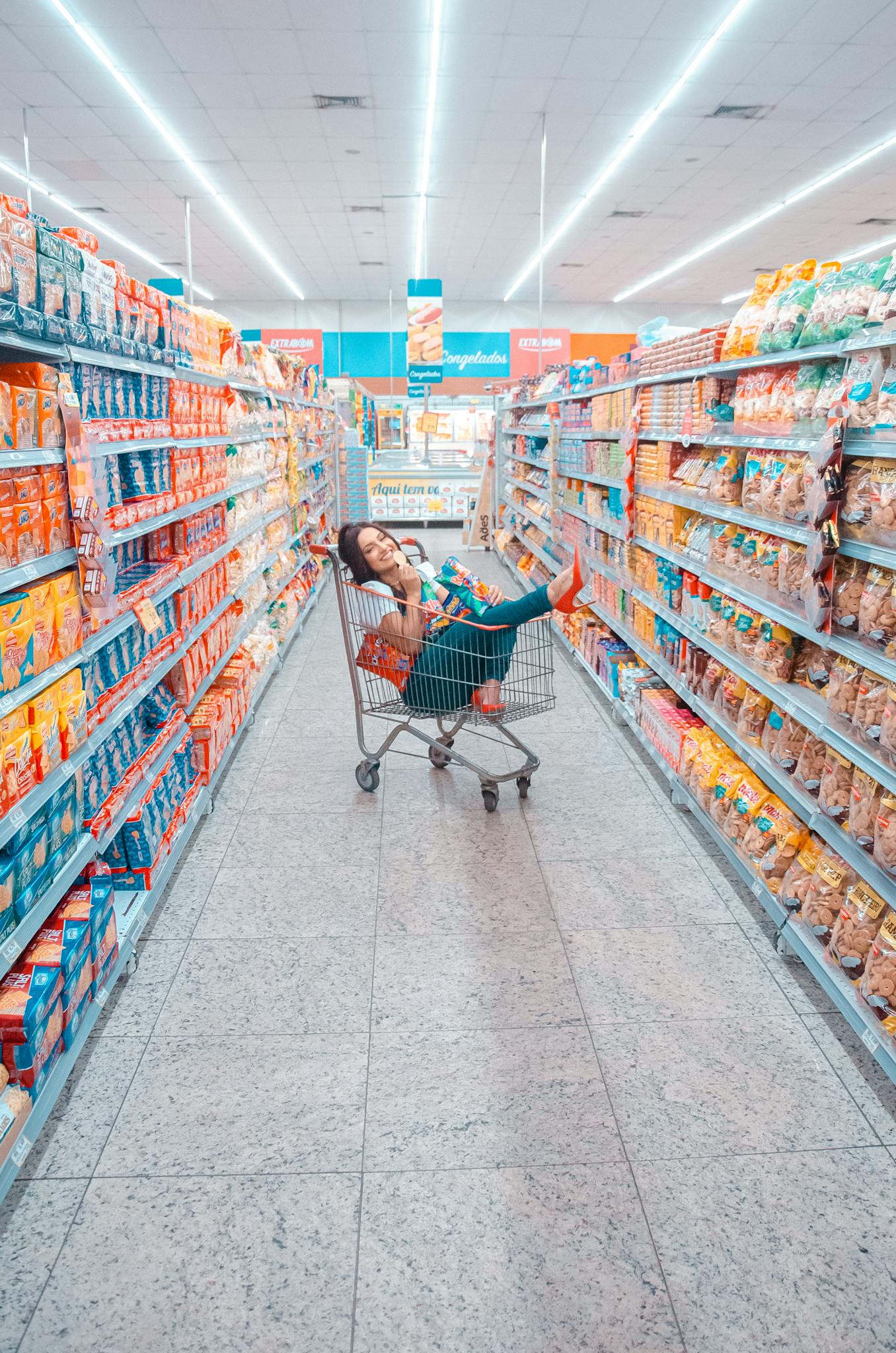Young woman enjoying a playful moment inside a supermarket shopping cart.